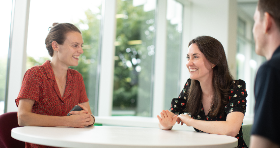 two women talking at a able looking over a man's shoulder in an AtkinsRelais iffice
